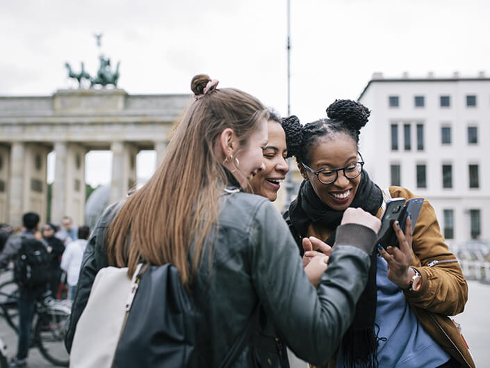 Three women smile while looking at a smartphone screen